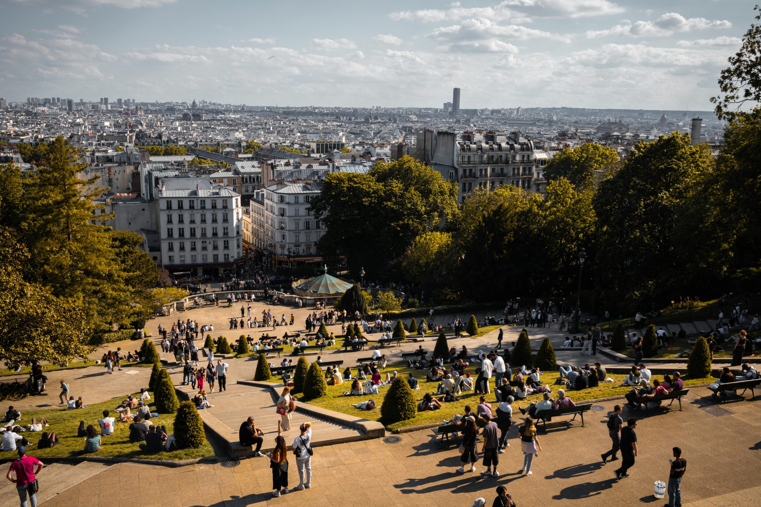 A bustling scene of people enjoying a sunny day at Montmartre with a panoramic view of Paris.